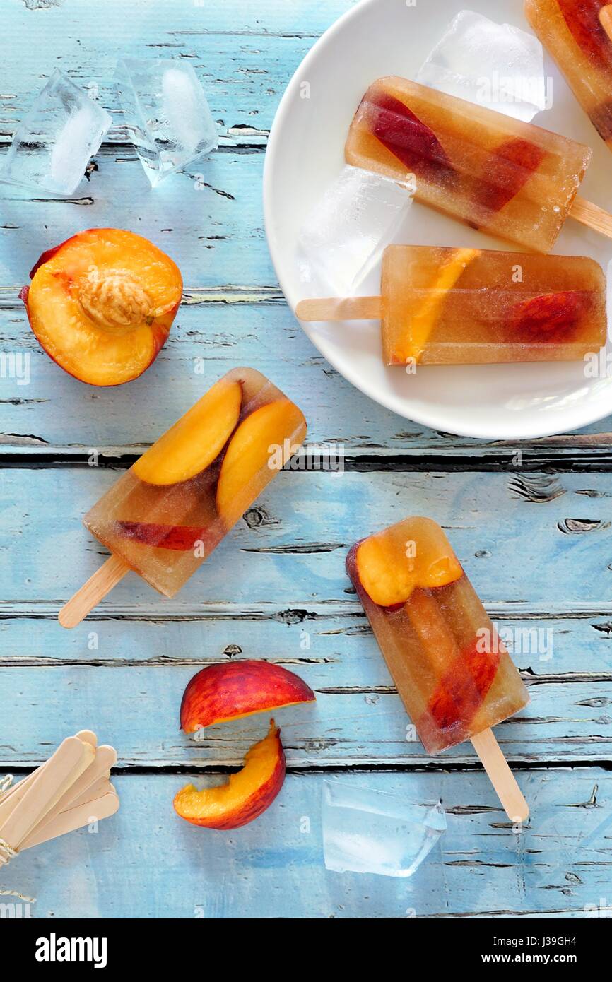 Homemade peach iced tea popsicles, overhead scene on rustic blue wood Stock Photo