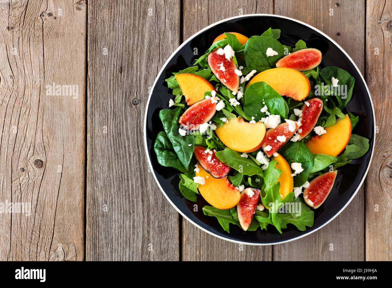 Autumn salad of arugula, spinach figs and goat cheese in a black plate, above view on a rustic