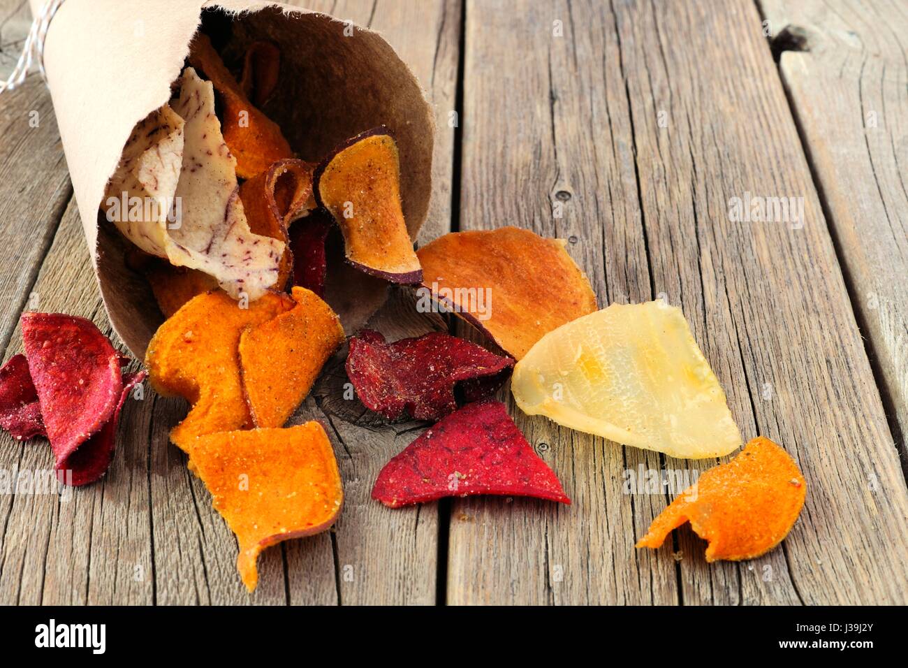 Healthy vegetable chips spilling from a paper cone on a rustic wooden background Stock Photo