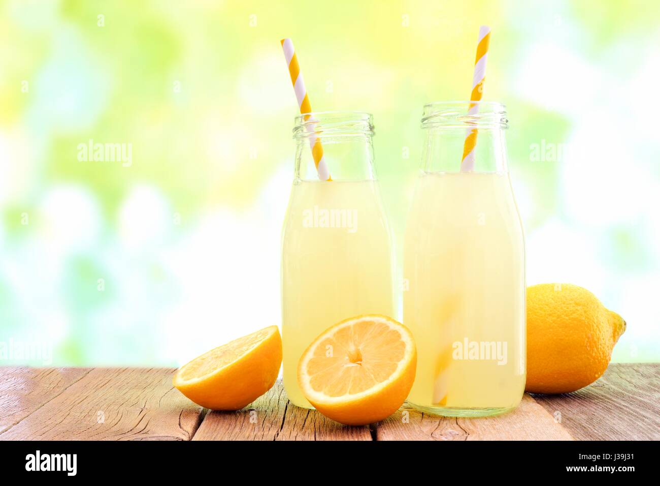 Two bottles of cold lemonade with lemon slices and straws with de-focused outdoor background Stock Photo