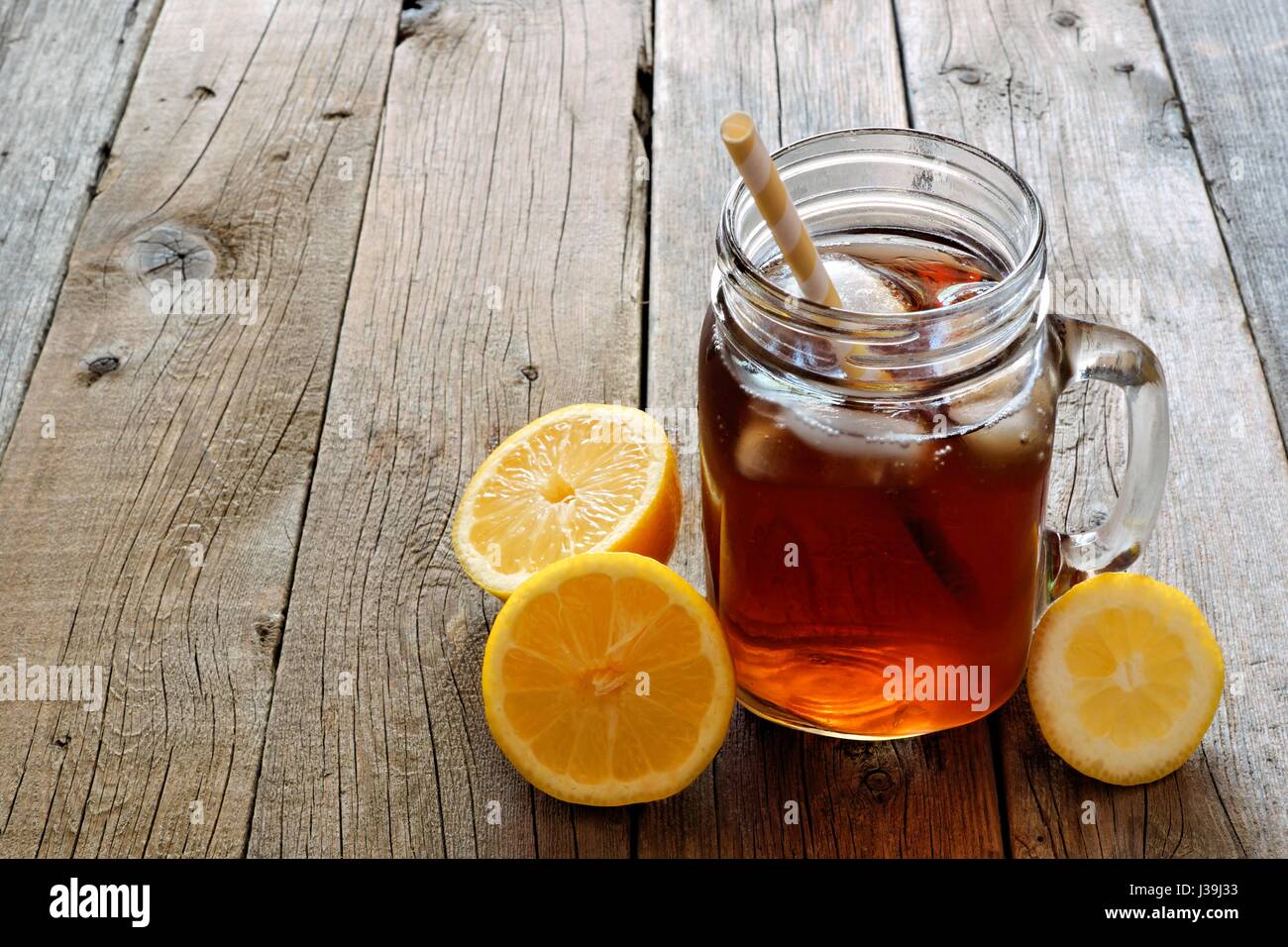 Mason jar glass of cold iced tea with lemon slices on a rustic wood background Stock Photo