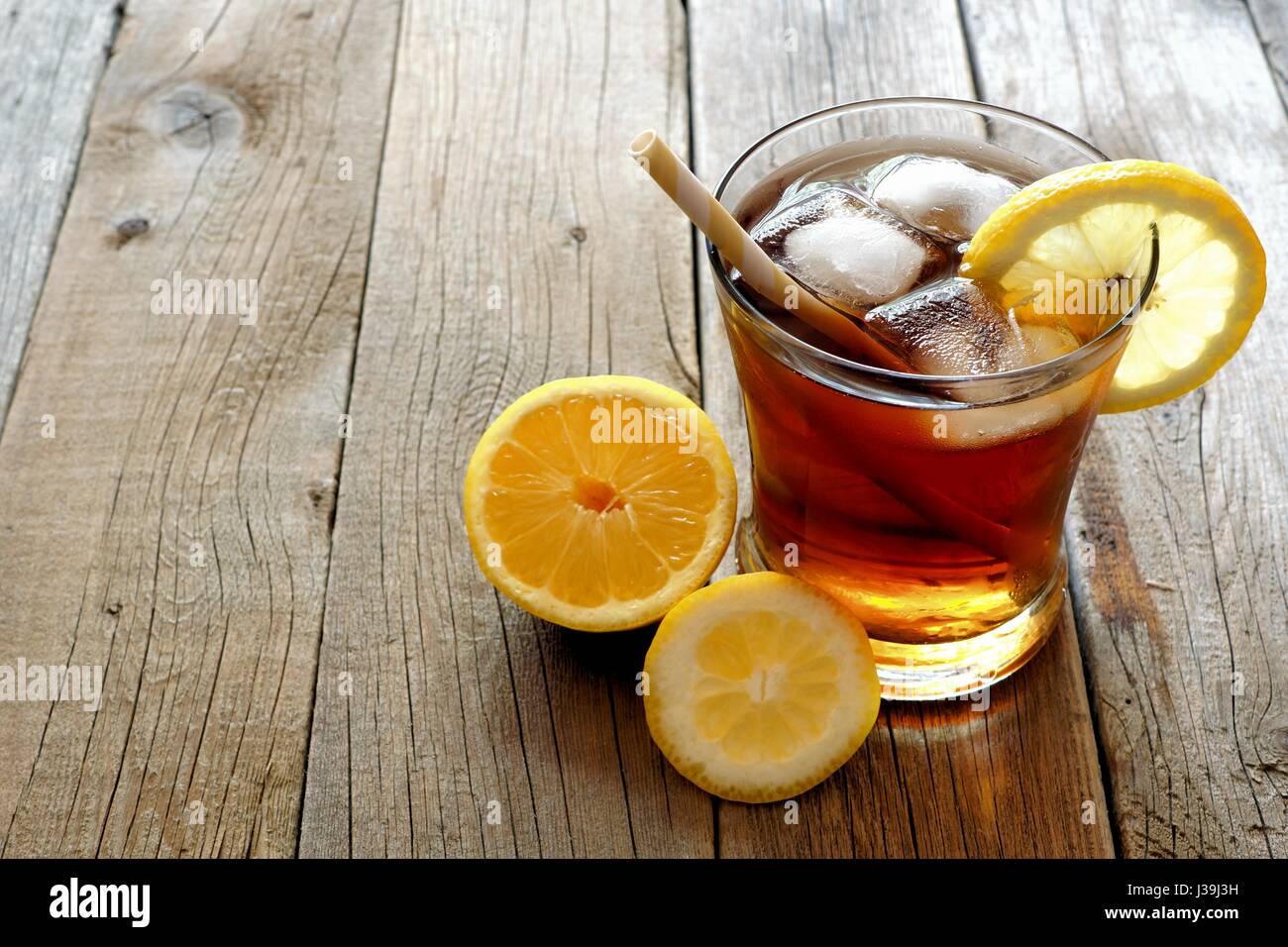 Glass of homemade lemon iced tea with straw on a rustic wooden background Stock Photo