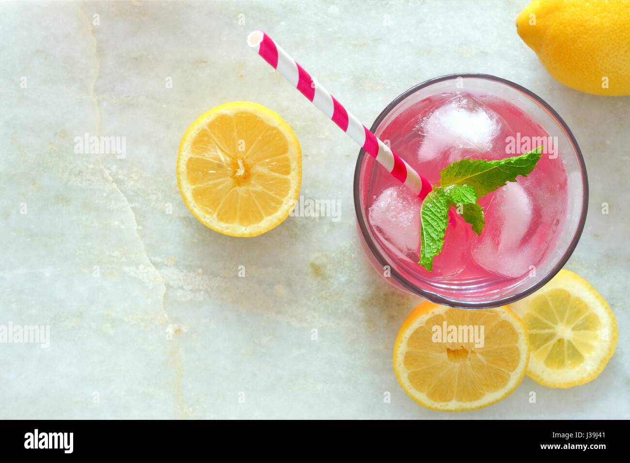 Glass of pink lemonade with mint and lemon slices overhead view on a white marble background Stock Photo