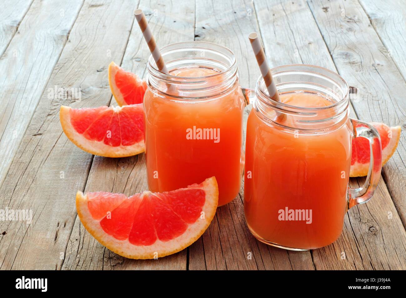 Two mason jar glasses of grapefruit juice with slices and straws on rustic wooden background Stock Photo