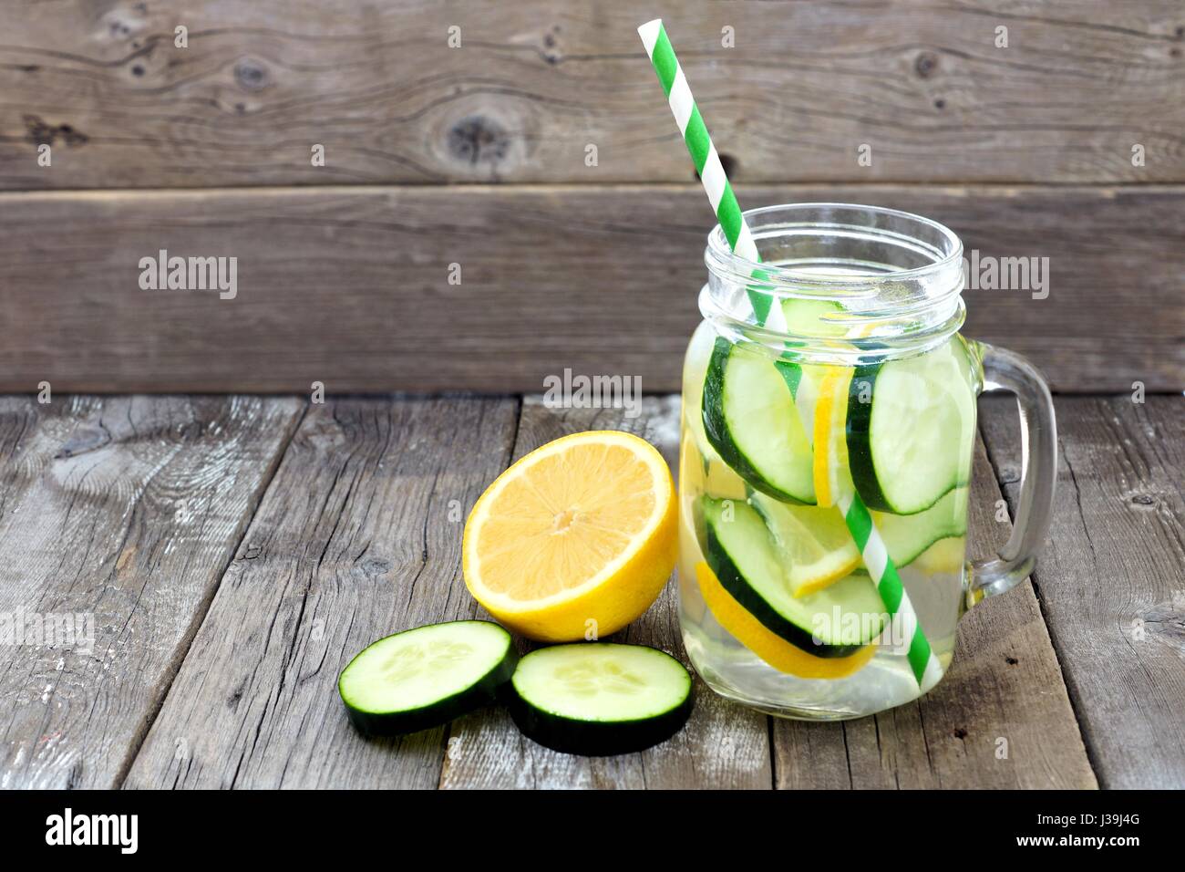 Lemon cucumber detox water in a mason jar glass with straw and slices against a rustic wood background Stock Photo