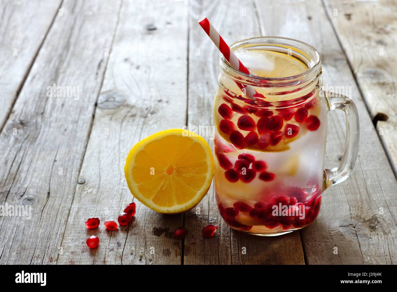 Pomegranate lemon detox water in a mason jar with straw against a rustic wood background Stock Photo