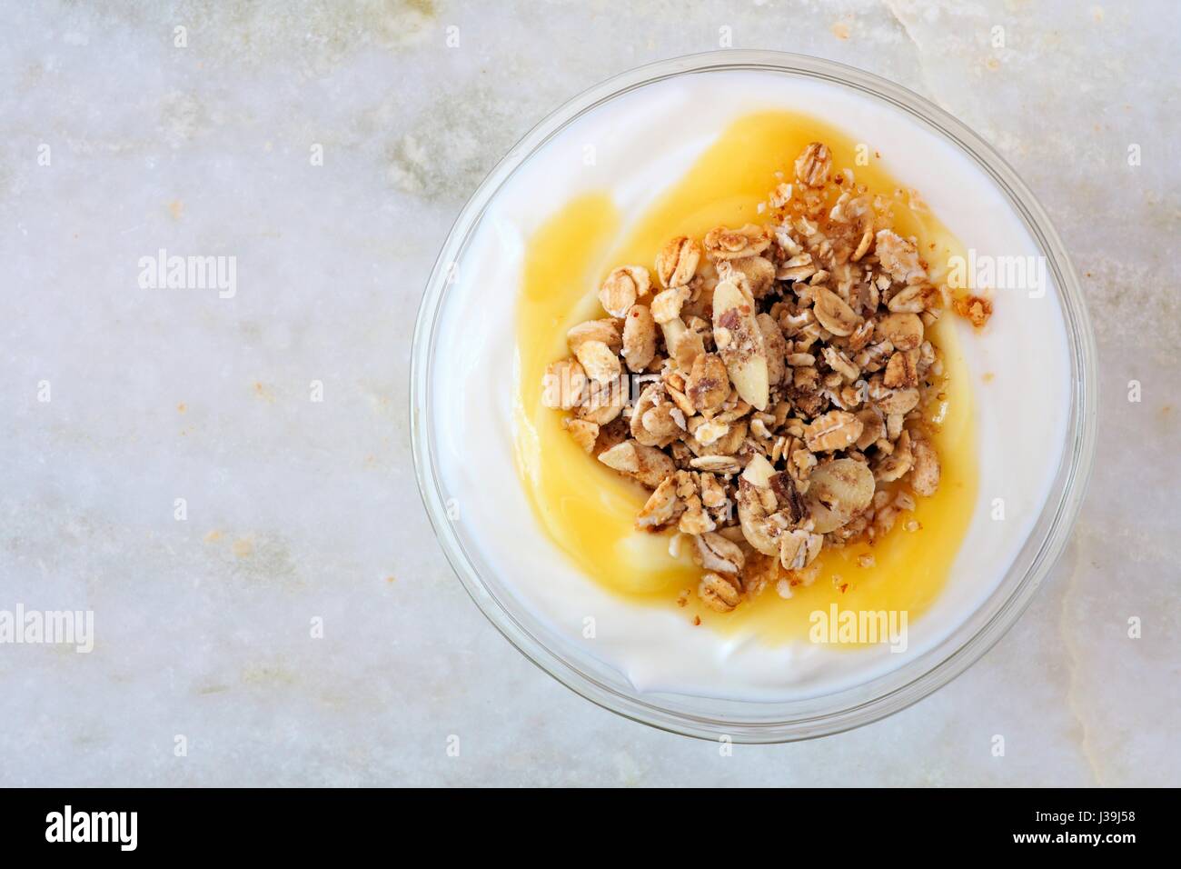Lemon flavored yogurt with granola, overhead view on white marble