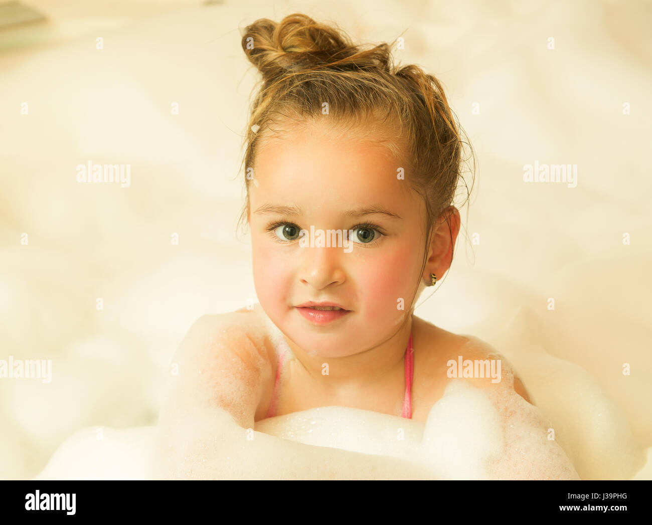 little beautiful girl posing inside of a bathtub with water and foam in