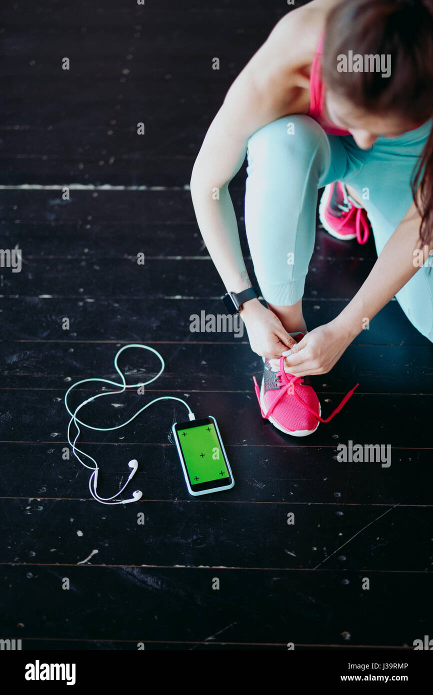 Runner woman tying running shoes laces getting ready for race on run track with smartphone and earphones for music listening on mobile phone. Athlete  Stock Photo