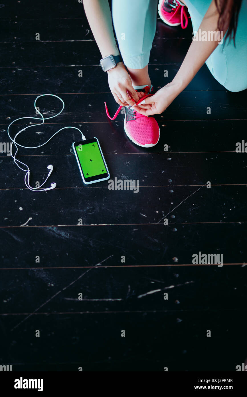 Runner woman tying running shoes laces getting ready for race on run track with smartphone and earphones for music listening on mobile phone. Athlete  Stock Photo