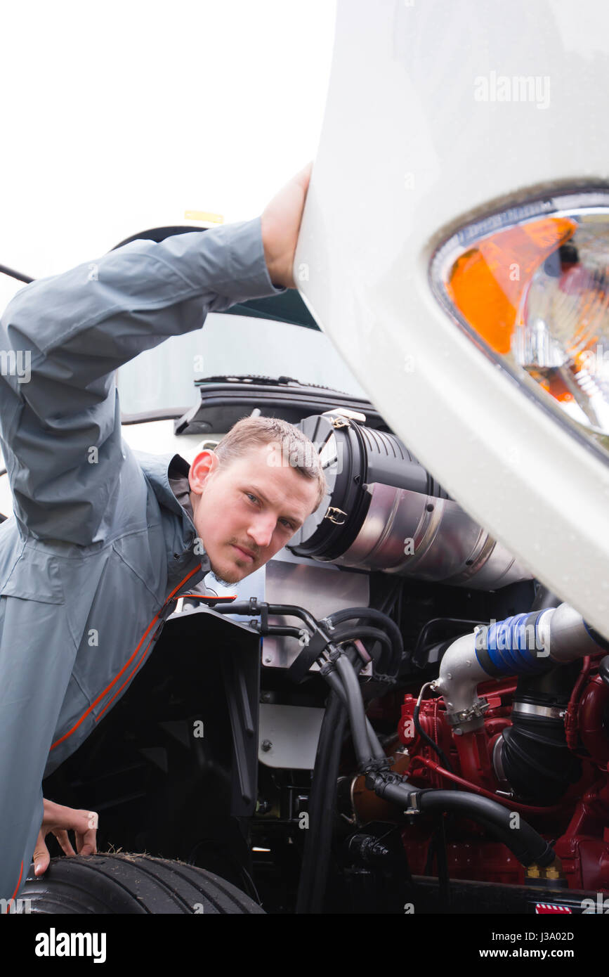 Inspector man checks diesel engine of commercial modern white big rig semi truck with the open hood for compliance with technical norms and standard Stock Photo