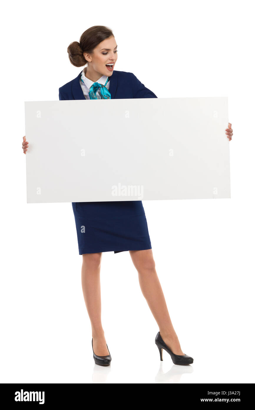 Young woman in blue formalwear and high heels, holding blank placard and reading. Front view. Full length studio shot isolated on white. Stock Photo