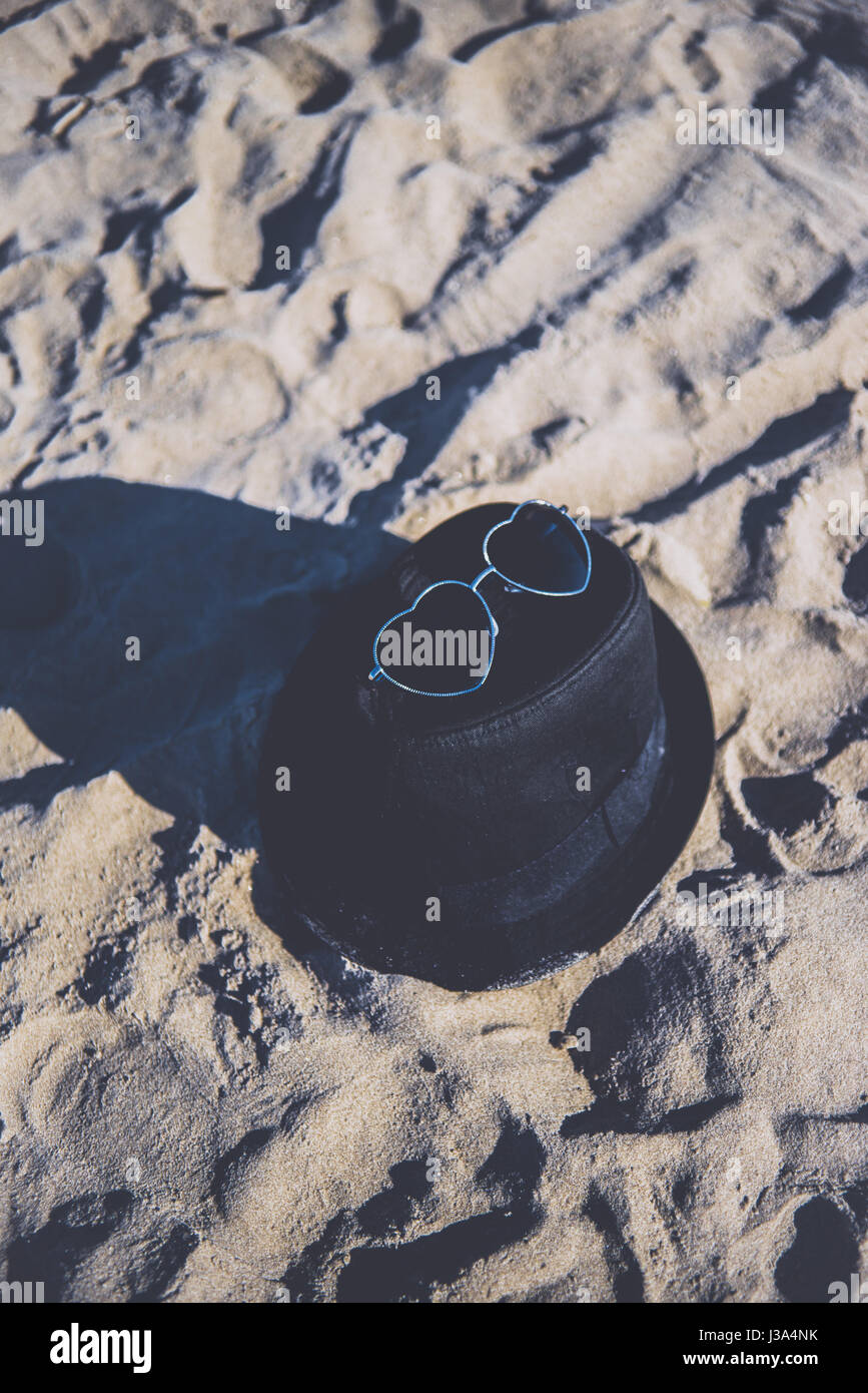 Woman's black felt hat and pair of sunglasses left on a beach Stock Photo
