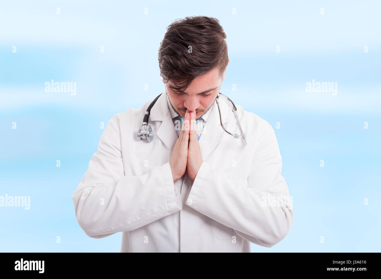 Male medic praying with hands clasped and eyes closed isolated on blue background Stock Photo