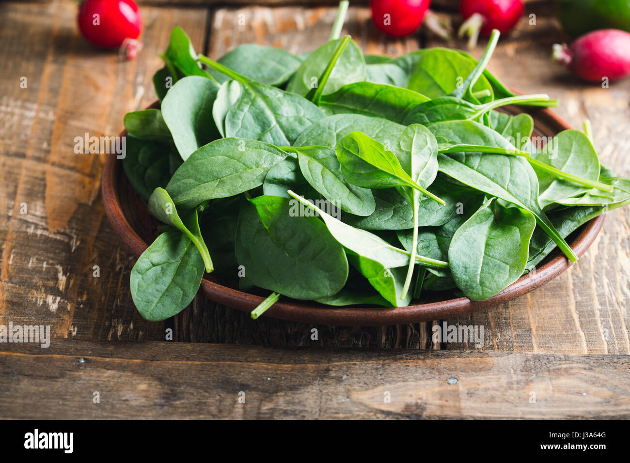 Fresh baby spinach leaves in rustic ceramic bowl Stock Photo