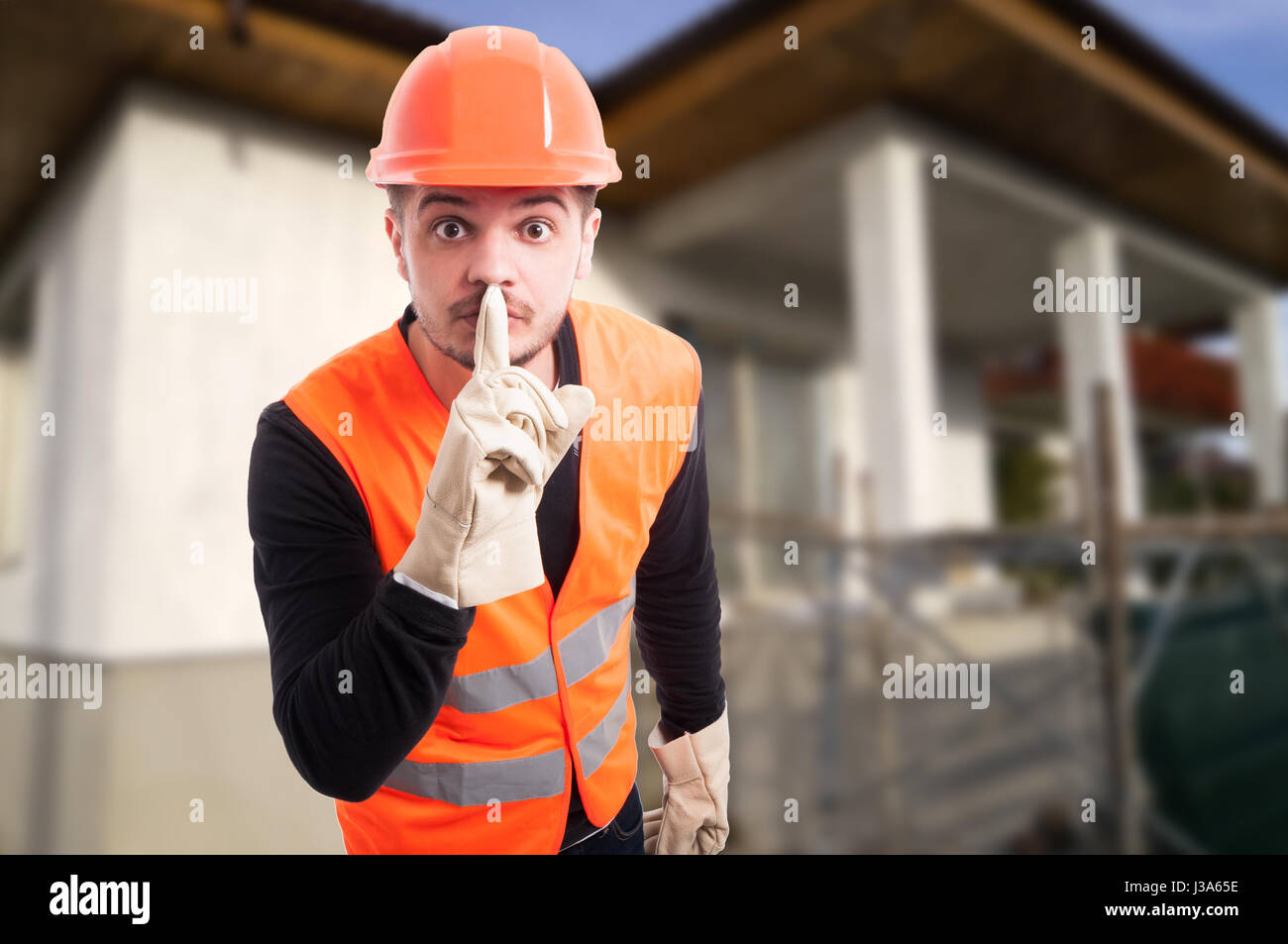 Male construction worker shushing after telling a secret at workplace with copyspace Stock Photo