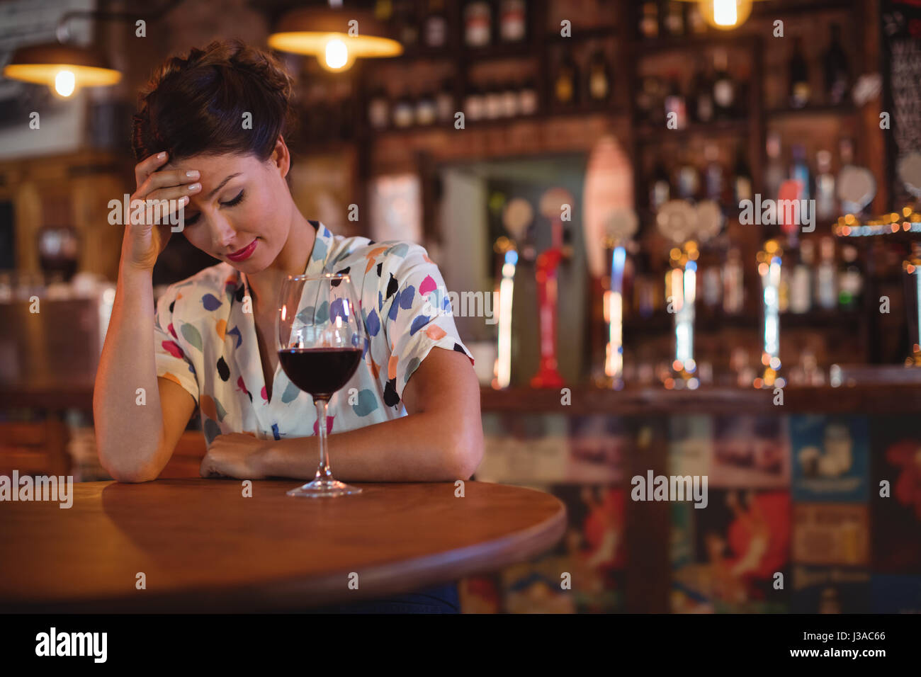 Upset woman sitting with hands on forehead in pub Stock Photo