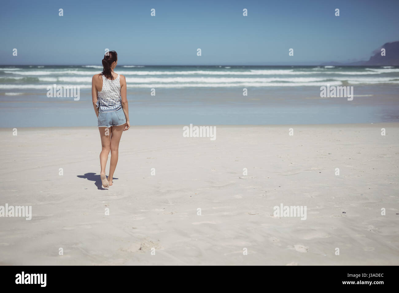 Rear view of woman walking at beach during sunny day Stock Photo