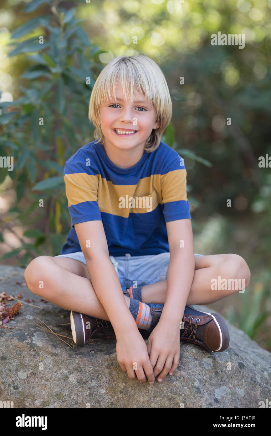 Portrait of smiling little boy sitting on rock in forest Stock Photo