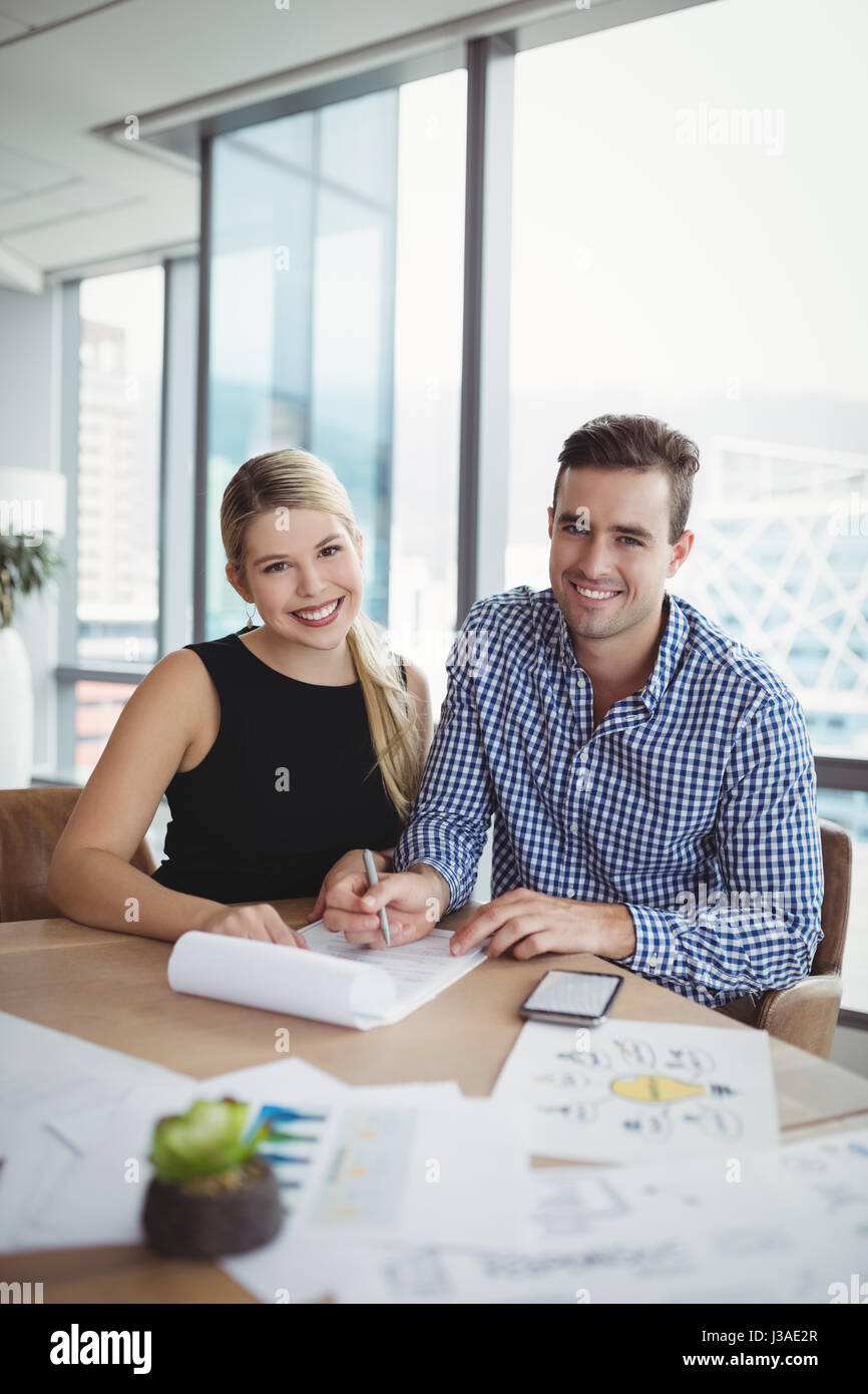 Portrait of smiling executives discussing over paper at desk in office ...