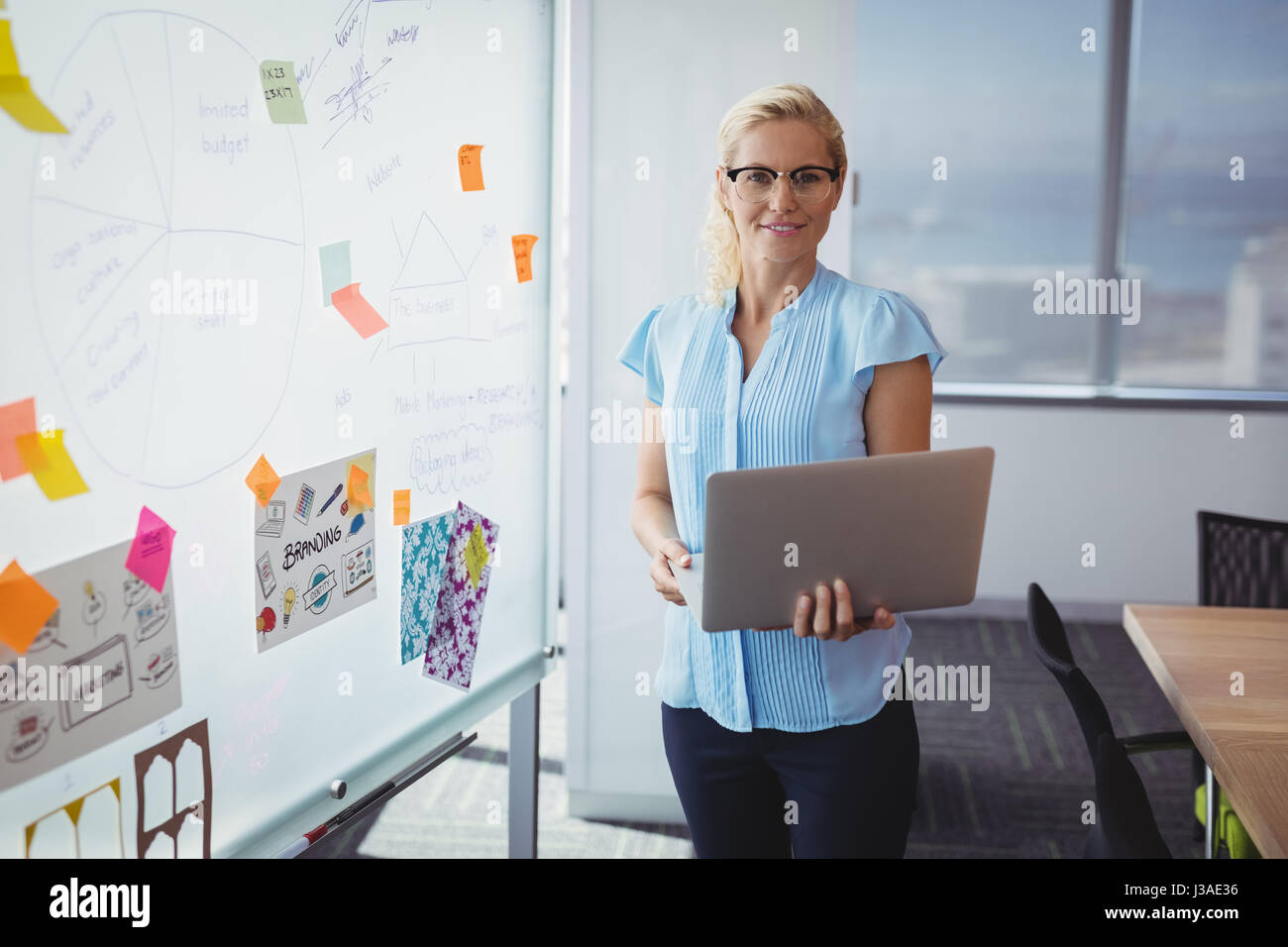 Portrait of smiling executive standing with laptop in office Stock ...
