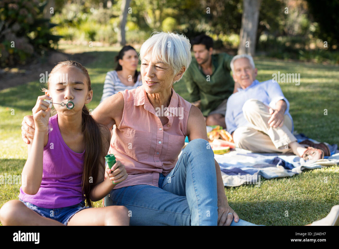 Grand mother looking at her granddaughter blowing bubbles in the park on a sunny day Stock Photo