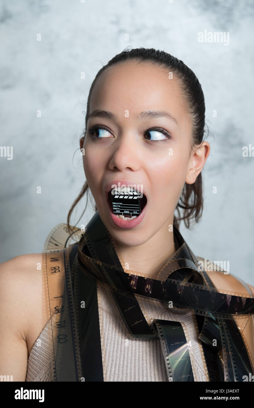 Young pretty woman funny portrait with movie filmstrip and little clapper board in her mouth Stock Photo