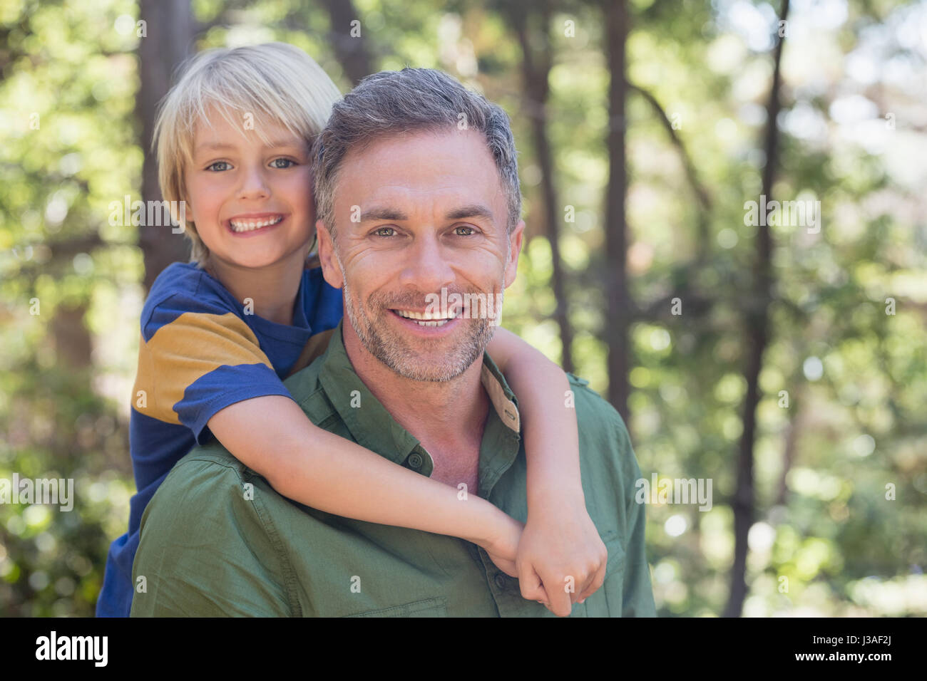 Portrait of smiling father piggybacking son in forest Stock Photo