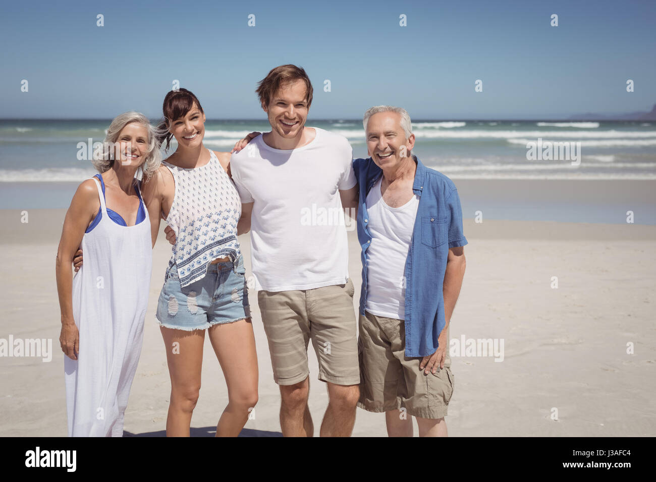 Portrait of happy family standing side by side at beach during sunny day Stock Photo