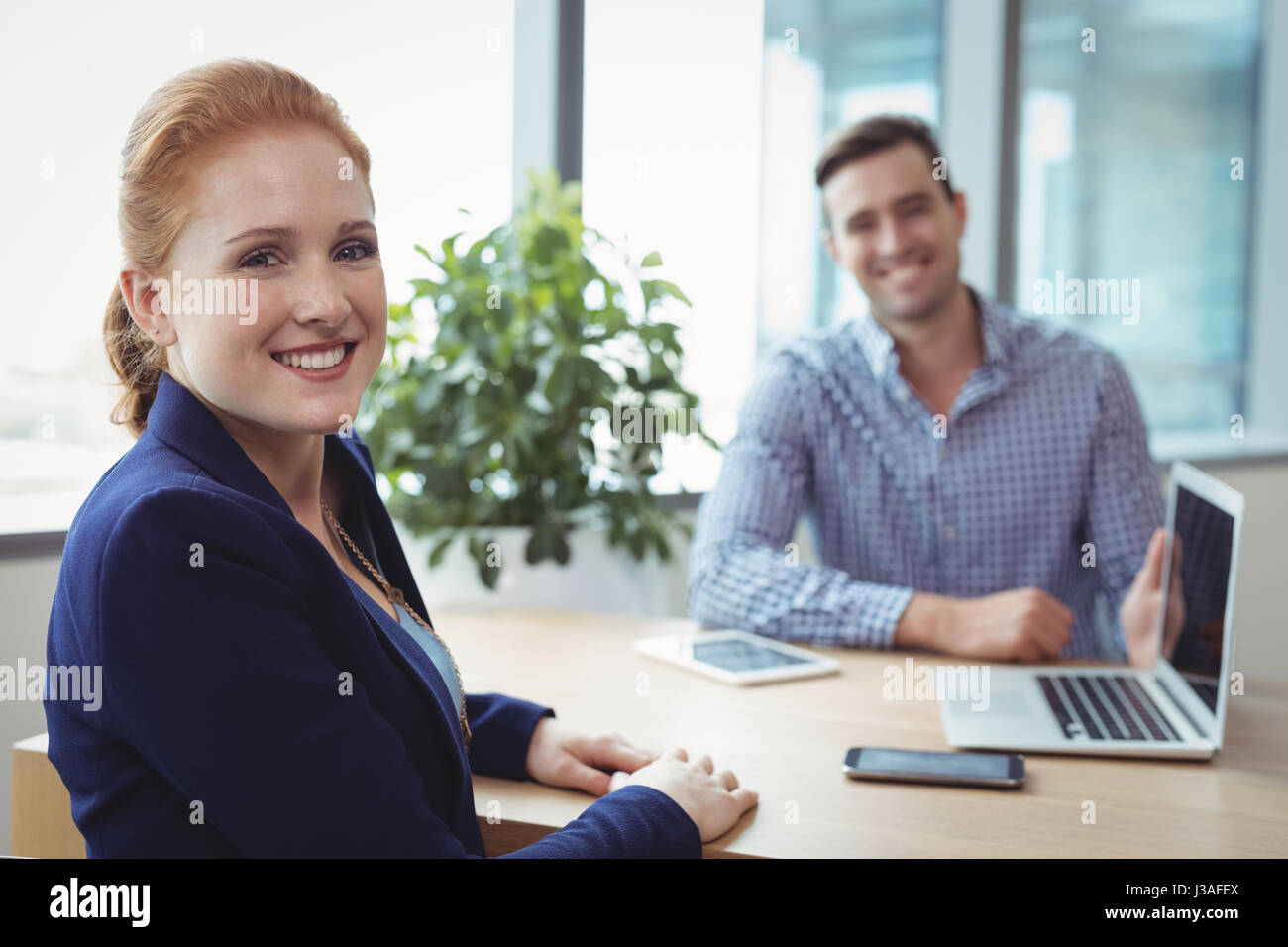 Portrait of smiling executives sitting at desk in office Stock Photo ...