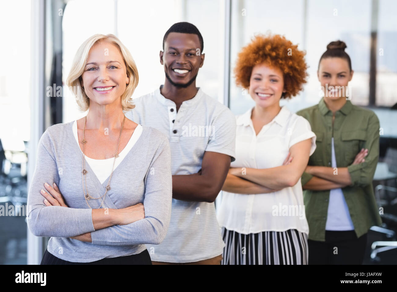 Portrait of smiling business people with arms crossed standing in row ...