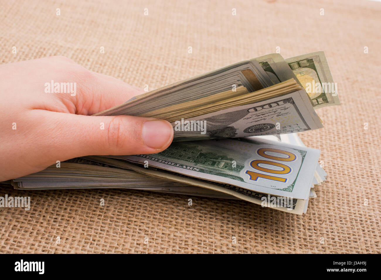 Hand holding banknote bundle of US dollar on a linen canvas background ...