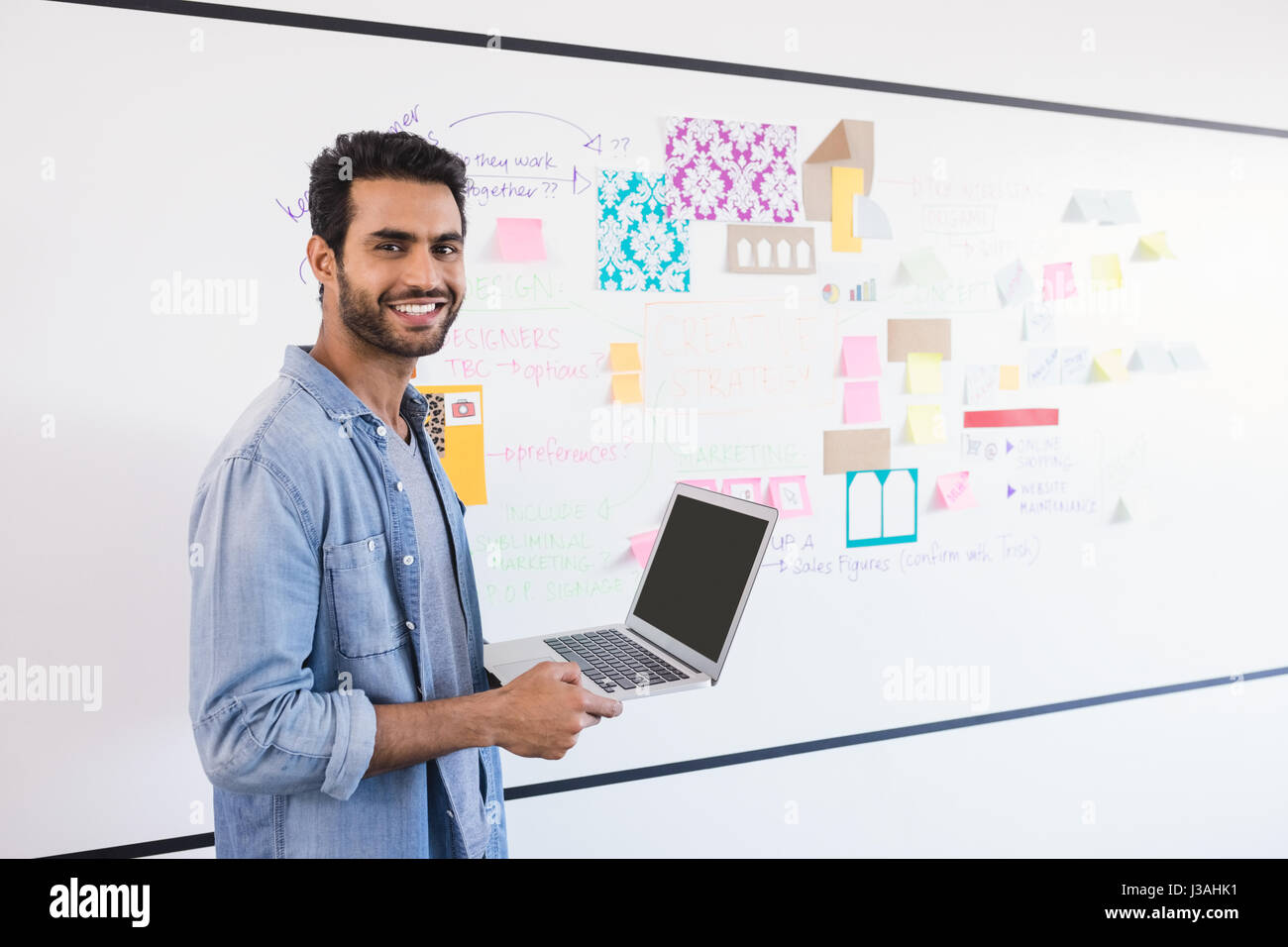 Portrait of businessman with laptop standing against whiteboard in office Stock Photo