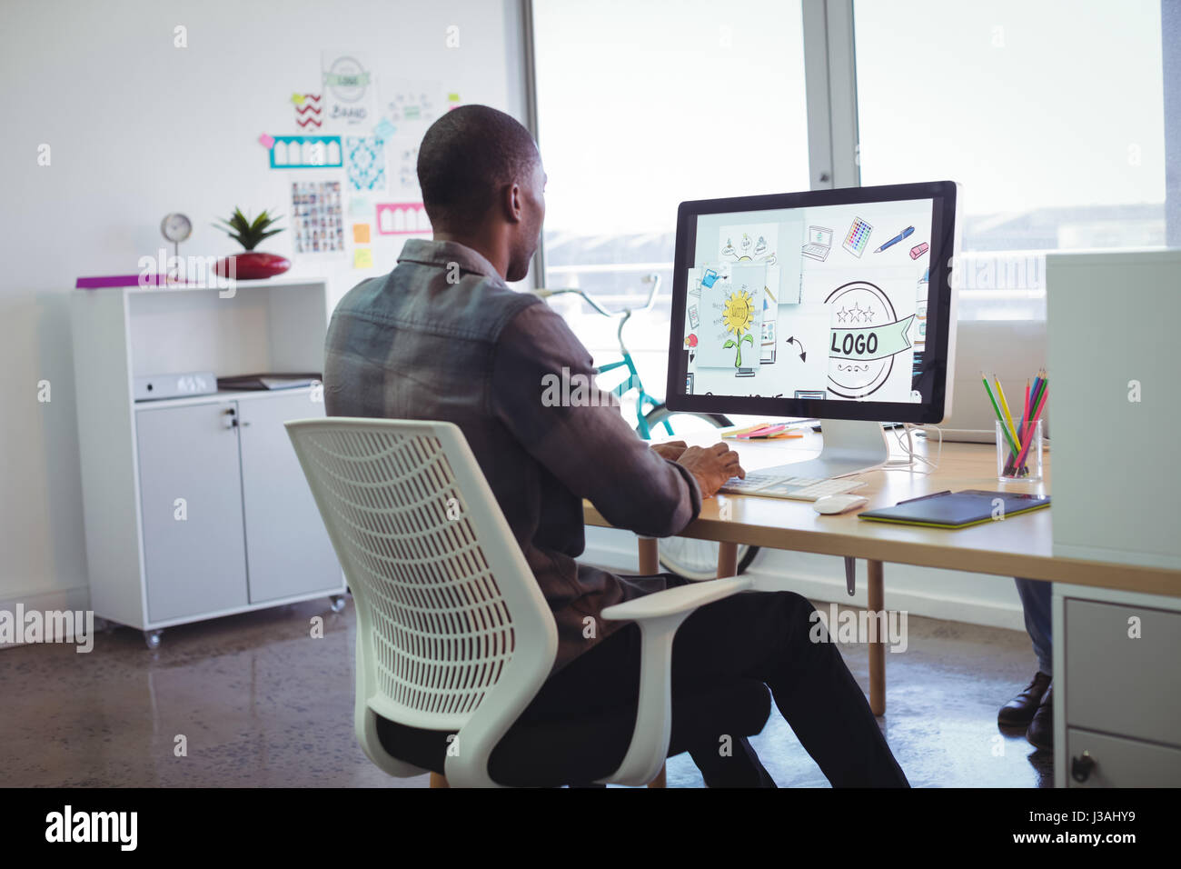 Rear view of businessman using computer in creative office Stock Photo ...