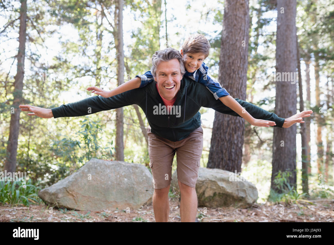 Portrait of cheerful father piggybacking son while hiking in forest Stock Photo