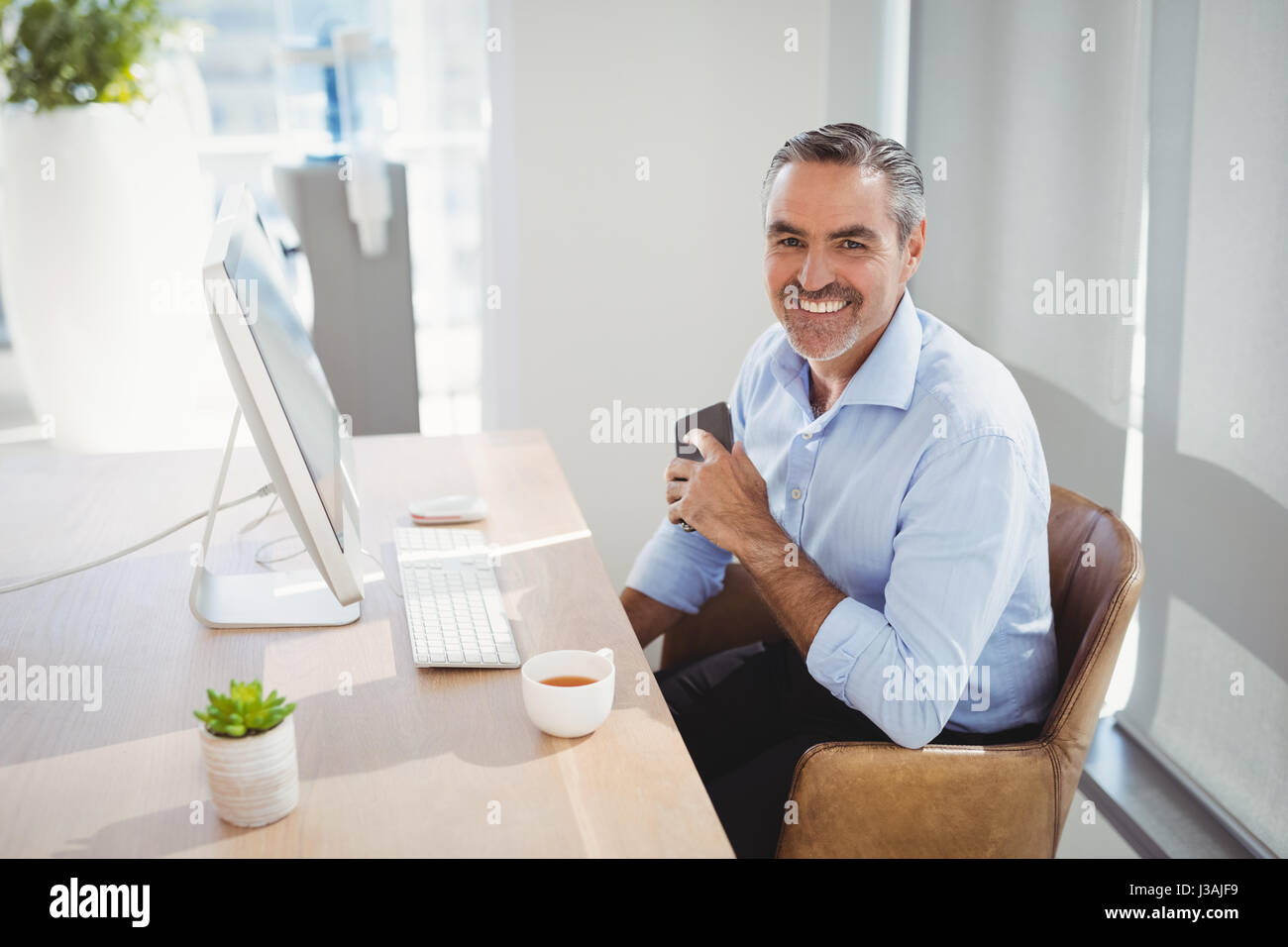 Portrait of smiling executive sitting at desk in office Stock Photo - Alamy