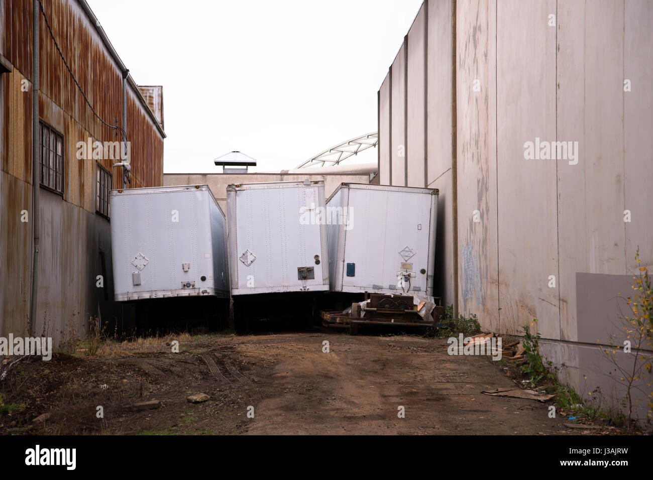 Place of the last parking of old dry van semi trailers between two old rusty industrial hangars in an industrial zone Stock Photo