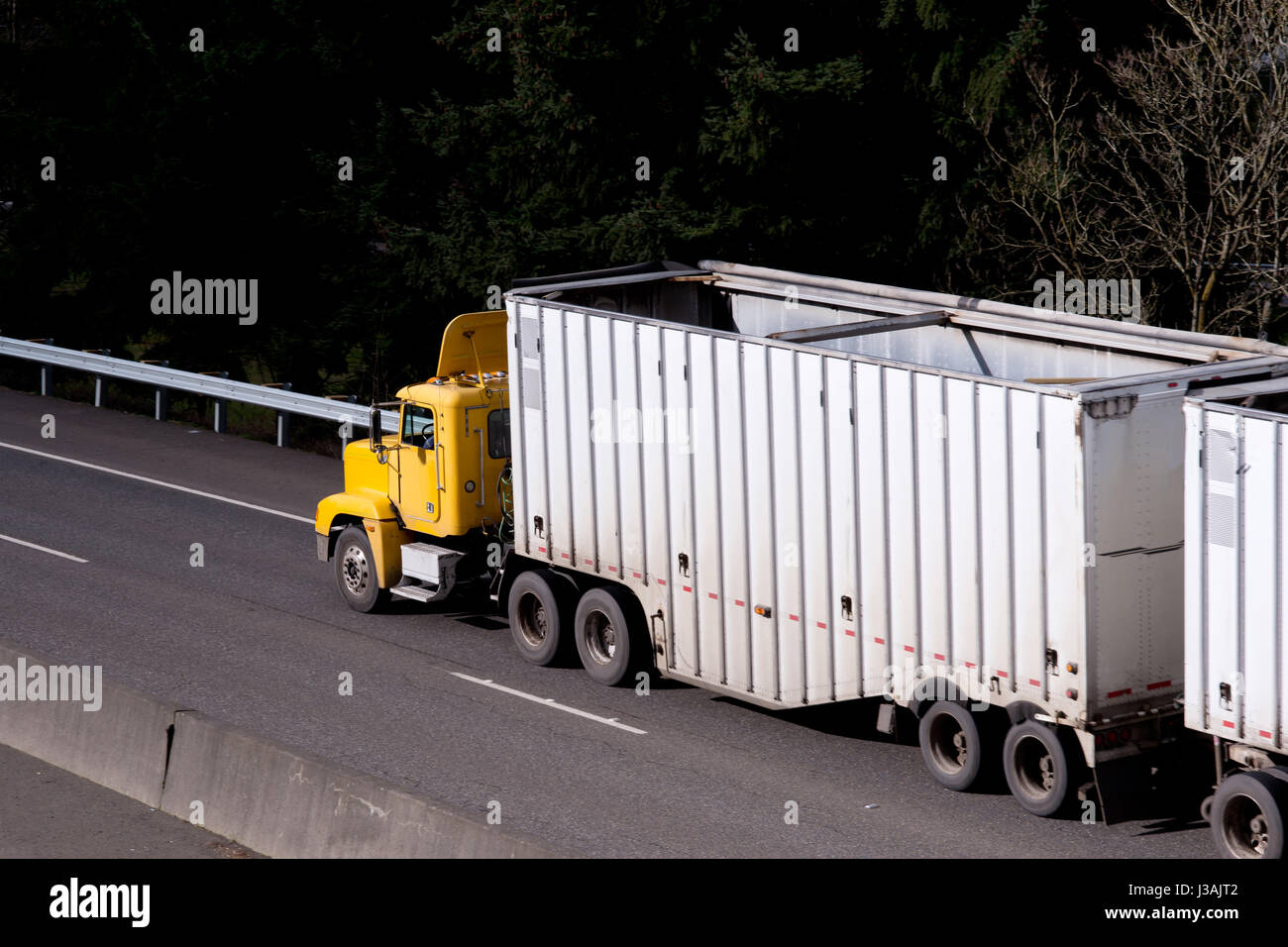 Professional Yellow powerful American semi truck for local transportation of commercial cargo is pulling open tandem trailers for bulk cargo Stock Photo