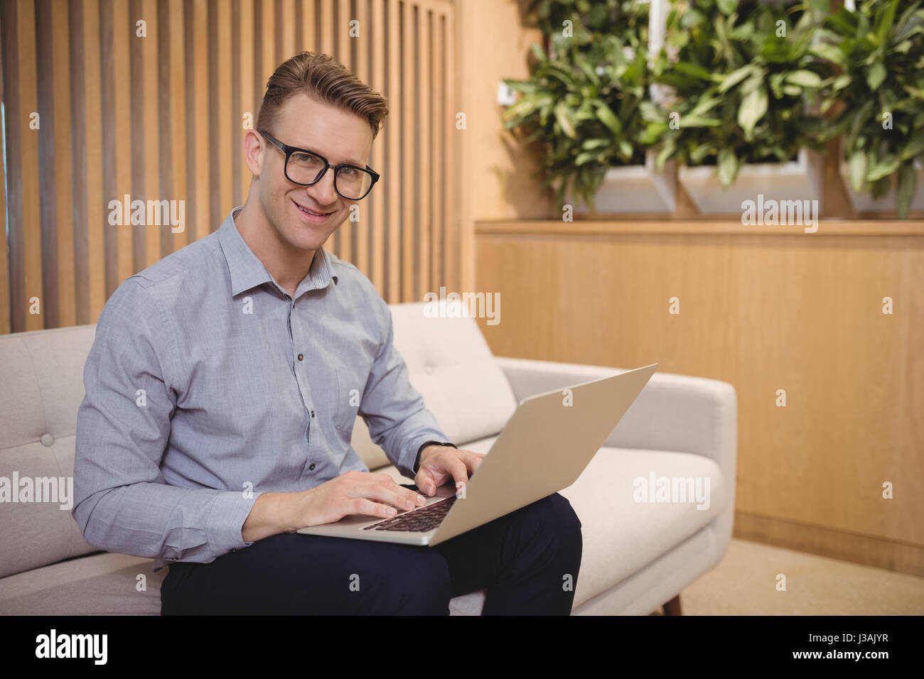 Portrait of smiling executive sitting on sofa and using laptop in ...