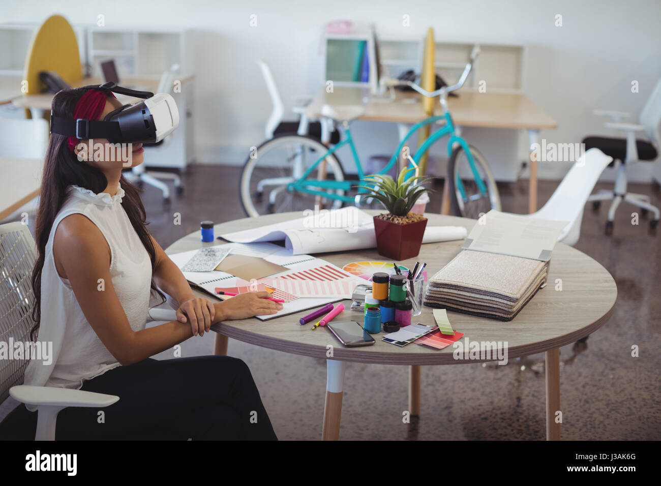 Businesswoman using virtual reality technology while sitting at desk in ...