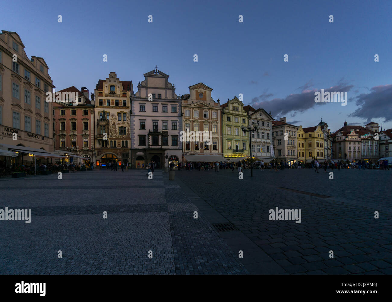 The lights come on, and tourists wander as night falls in Prague in the historic Old Town Square in the blue hour. Stock Photo