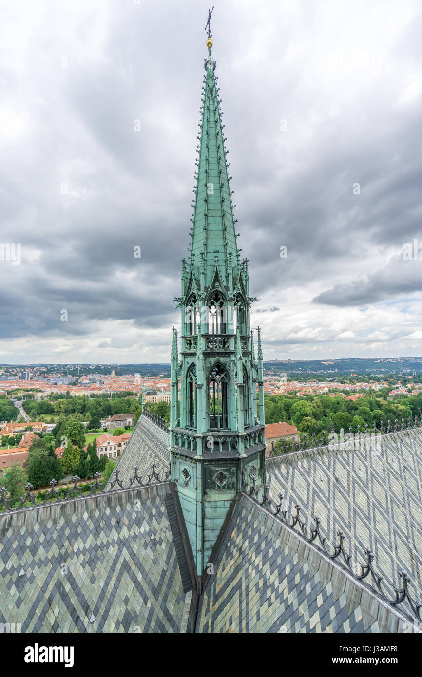 The copper bell tower and roof detail of the St Vitus Cathedral in Prague, with the cityscape in the background on a cloudy day. Stock Photo