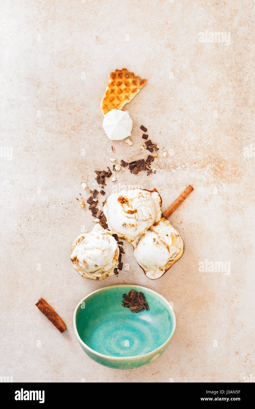 Ice cream with melting scoops, various ingredients and empty vintage bowl on rustic surface, flat lay Stock Photo