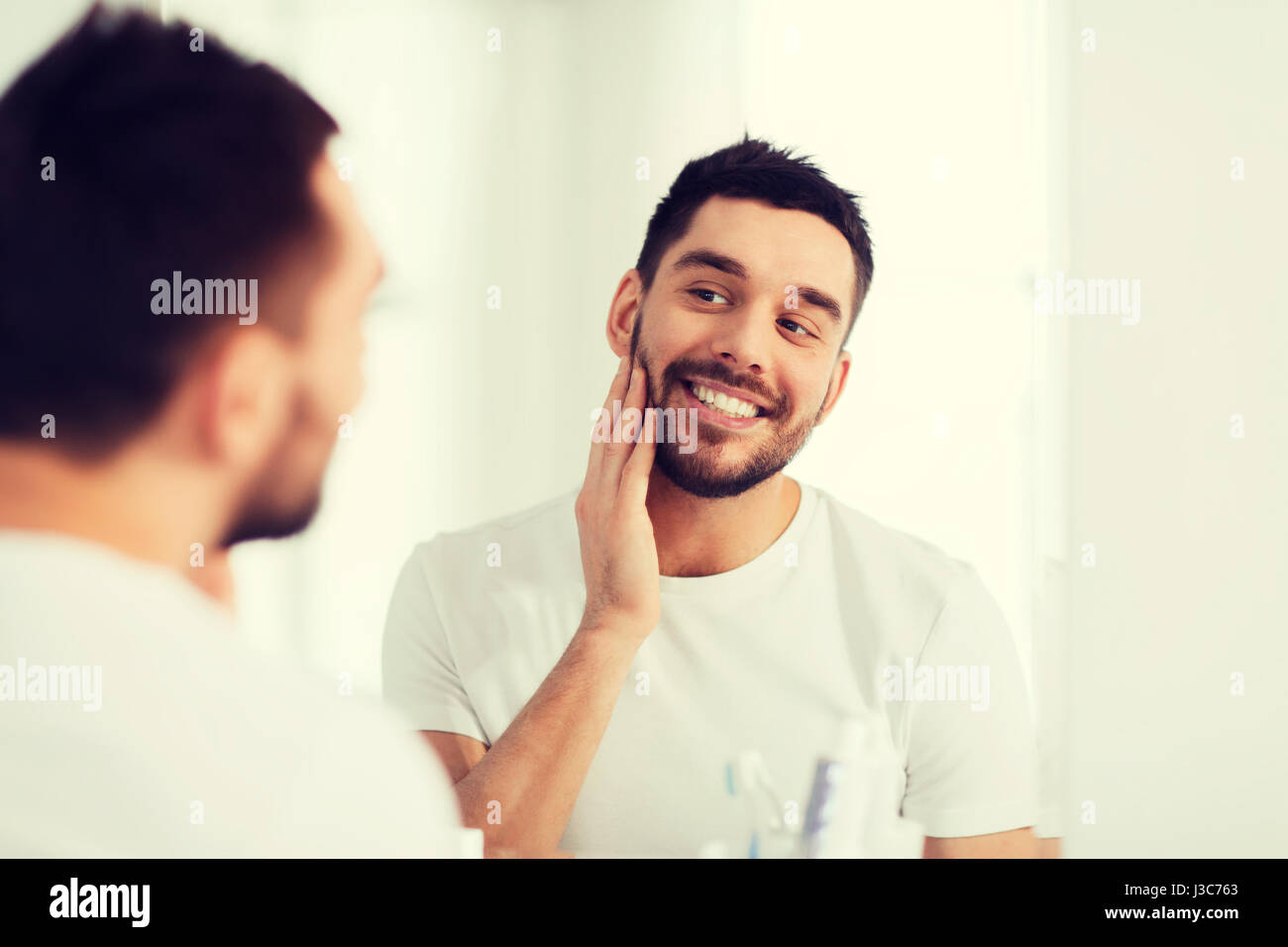 happy young man looking to mirror at home bathroom Stock Photo