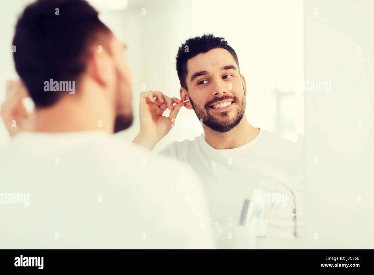 man cleaning ear with cotton swab at bathroom Stock Photo Alamy