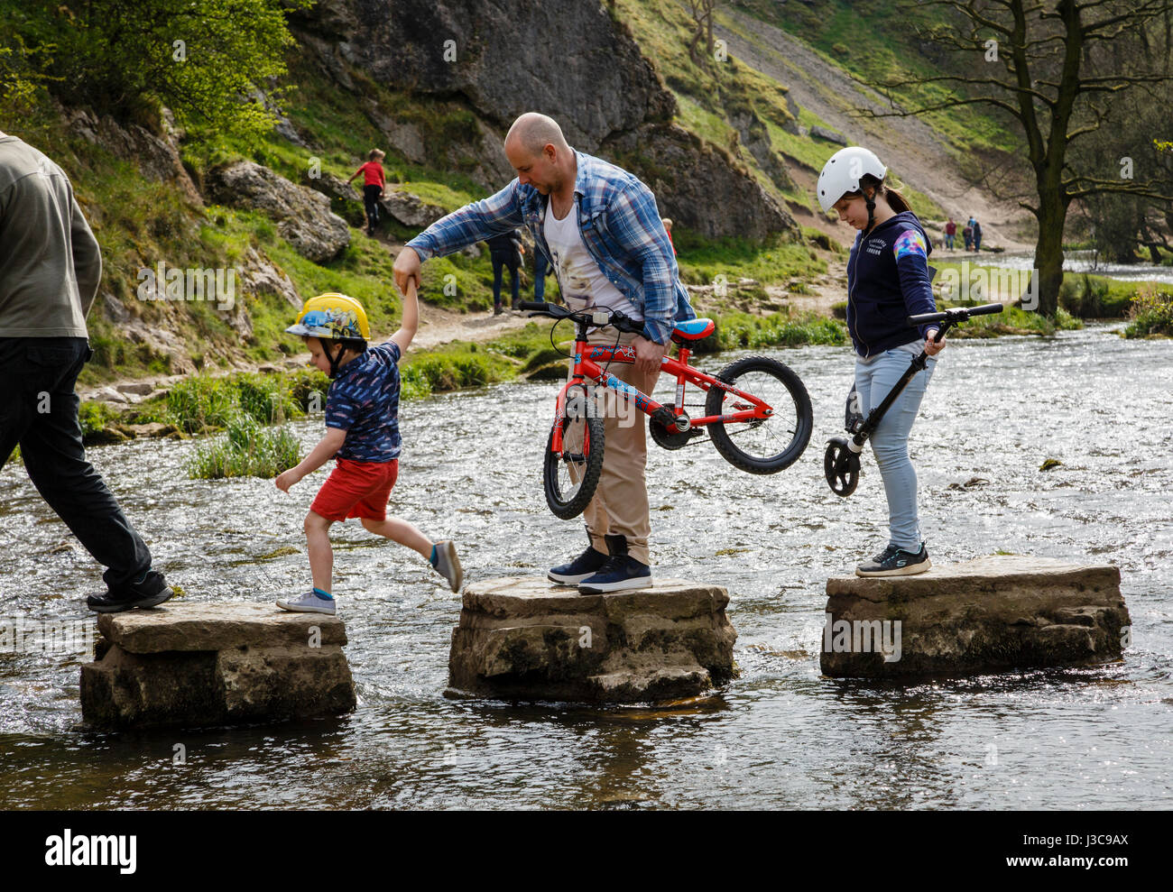 Dad helping his kids to cross the stepping stones at Dovedale, Peak District National Park, Derbyshire Stock Photo