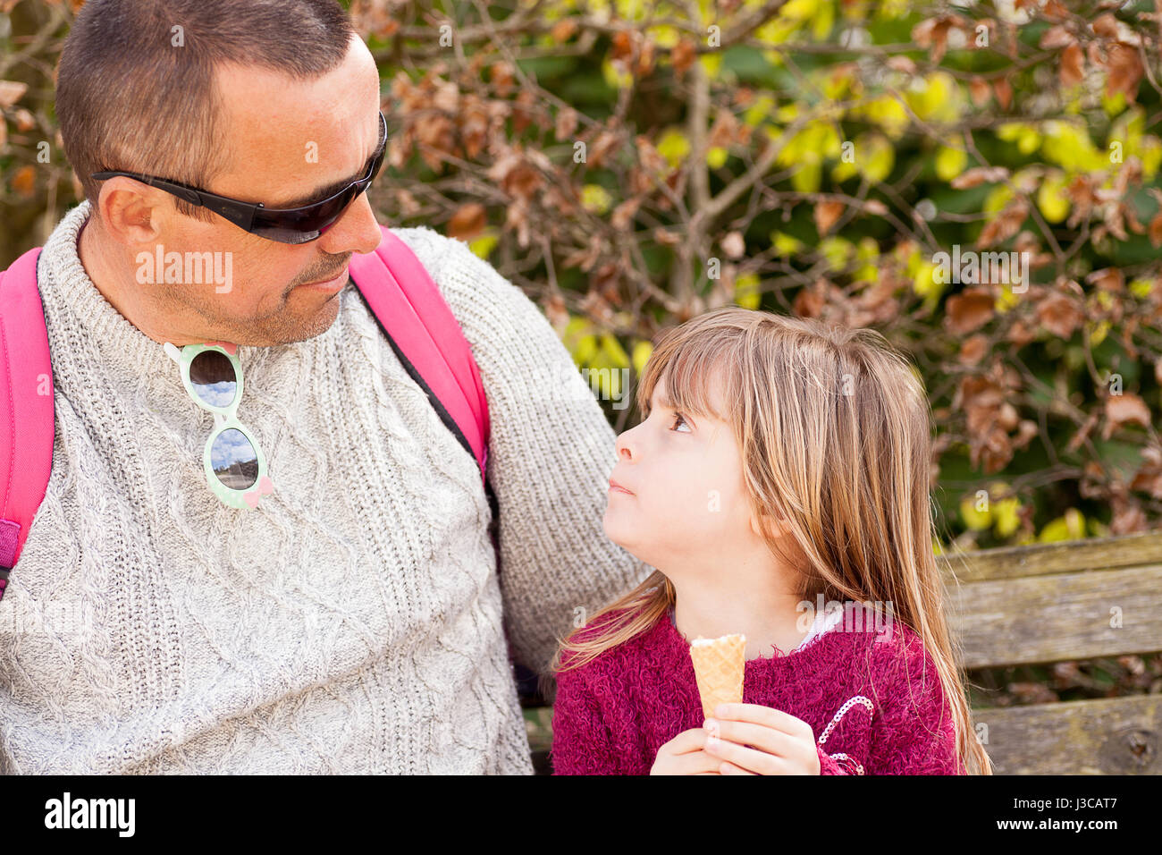 Real people. Man and little girl looking at each other. Father and daughter enjoying quality time outdoors with icecream. Candid family portrait. Stock Photo