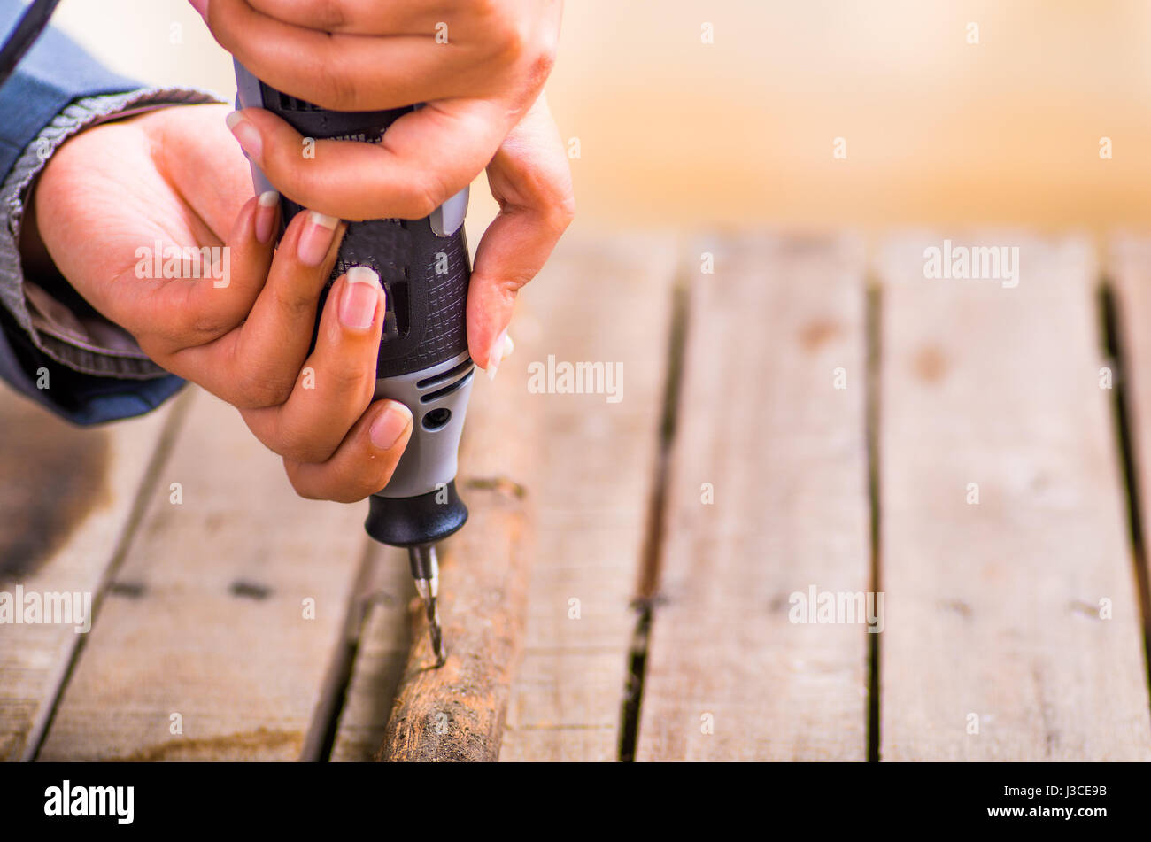 A closeup of a hardworker man drilling a wood stick with his drill on a wooden background Stock Photo