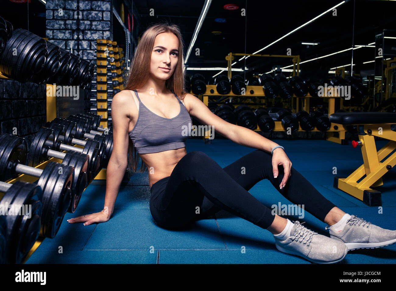 Young fitness girl sitting on the floor next to dumbbells in gym Stock ...