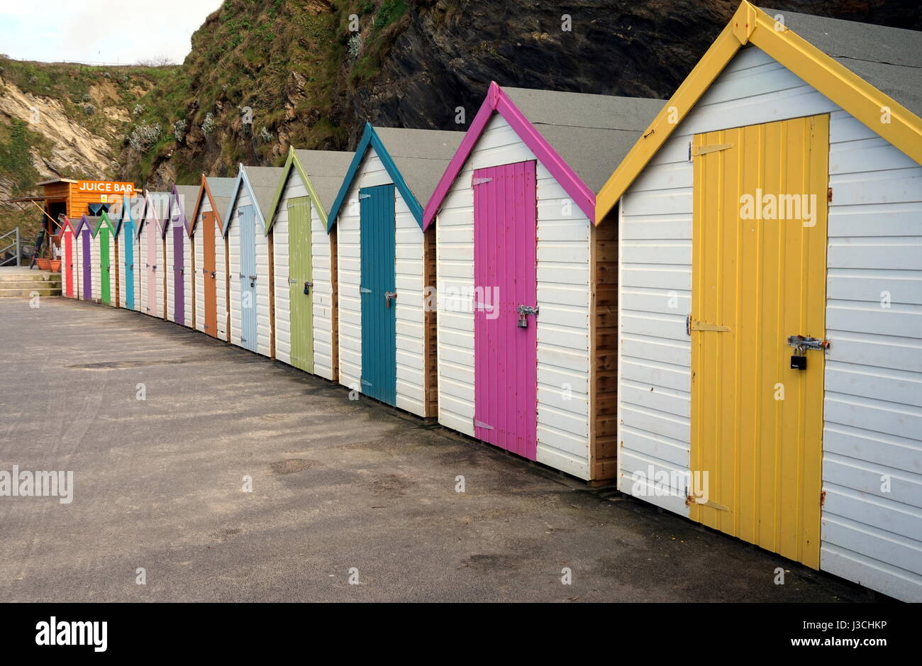 Row of colorful beach huts at the bottom of a rocky cliff on the sea shore Stock Photo